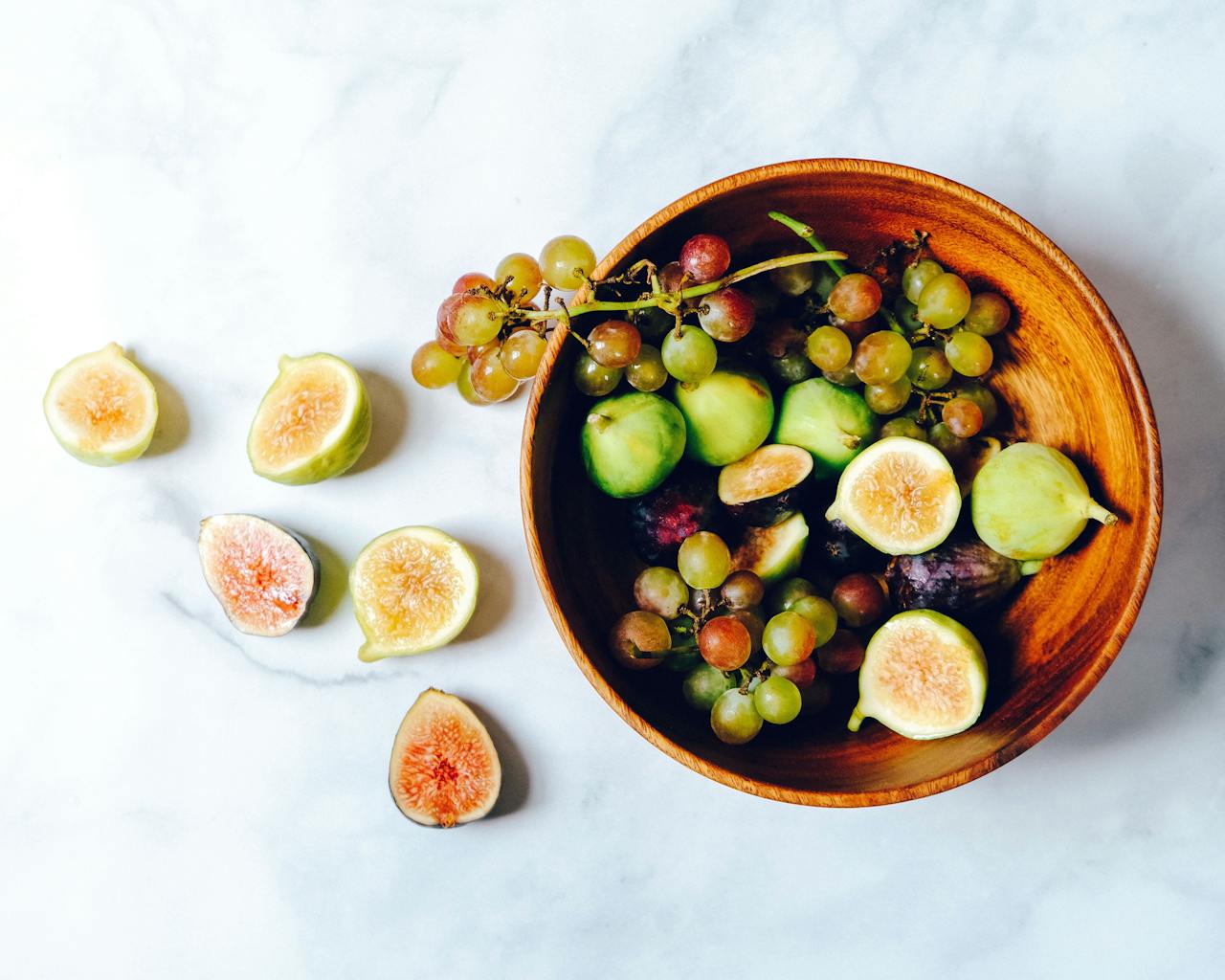 embark A vibrant and fresh bowl of green grapes and figs on a marble surface, perfect for healthy eating.