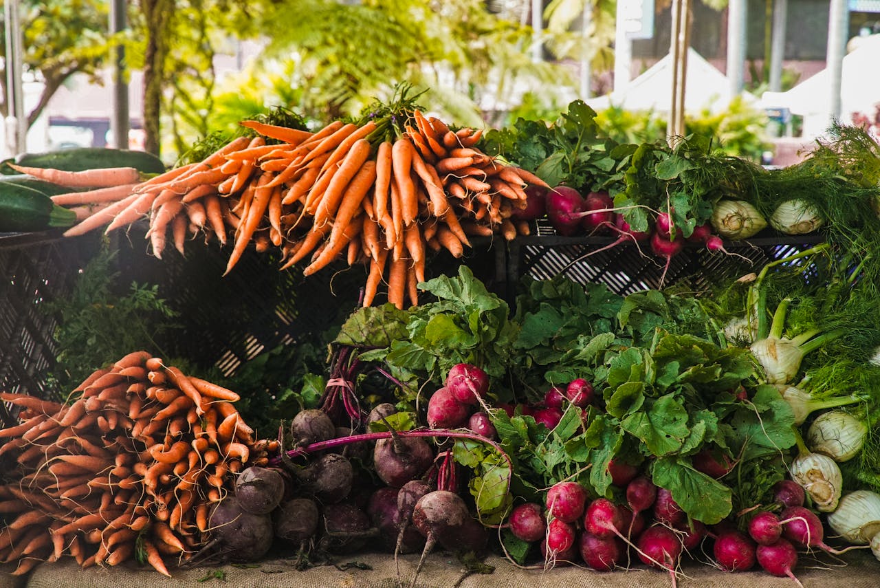 gallery-02 A vibrant display of fresh carrots, radishes, and greens at a local outdoor market.