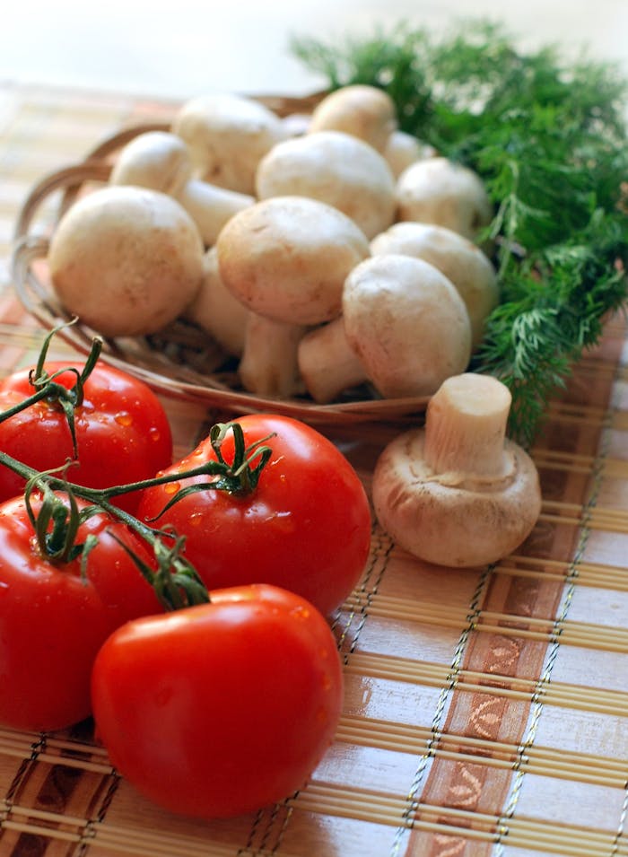 services-01 Close-up of fresh tomatoes and mushrooms on a rustic wooden mat, ideal for healthy cooking.