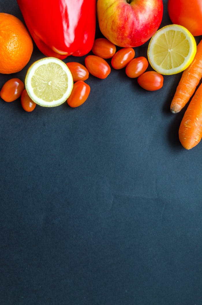 gallery-06 Colorful arrangement of fresh produce including citrus, carrots, and tomatoes on a dark backdrop.