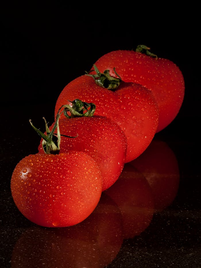 our-story A row of fresh tomatoes with water droplets against a dark background.